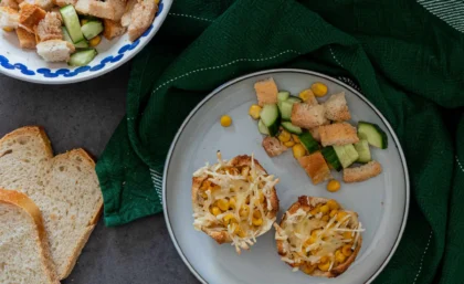 Einfache und schnelle Toast-Törtchen mit Mais und veganem Käse auf einem Teller. Daneben liegt Gurkensalat.