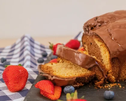 Fertiger Becherkuchen mit Joghurt, übergossen mit Schokolade und zwei Stücke abgeschnitten. Diese liegen daneben, genauso wie Erdbeeren und Blaubeeren.