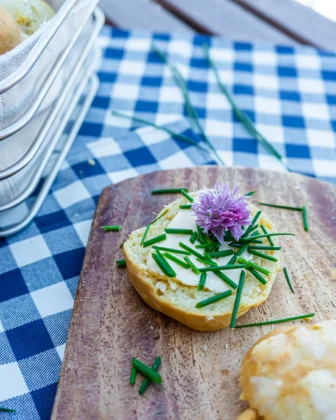 Ein Cheese Scone mit Butter und Schnittlauch liegt auf einem Brettchen.