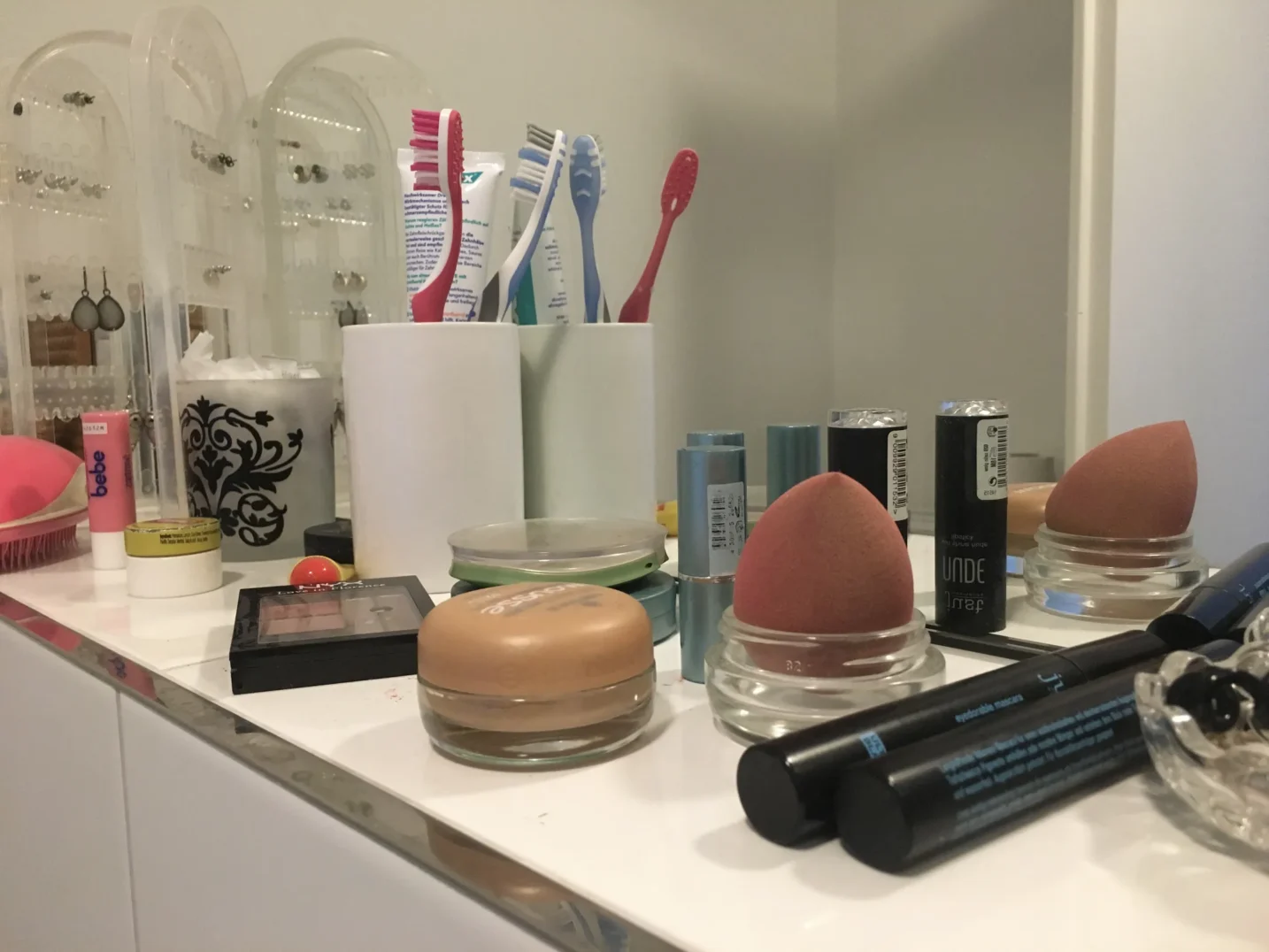 Ein Einblick in mein Badezimmer bevor ich Zero Waste in meinem Leben umgesetzt habe. Es stehen konventionelles Make up, Zahnbürsten und Zahnpasta vor einem Spiegel.