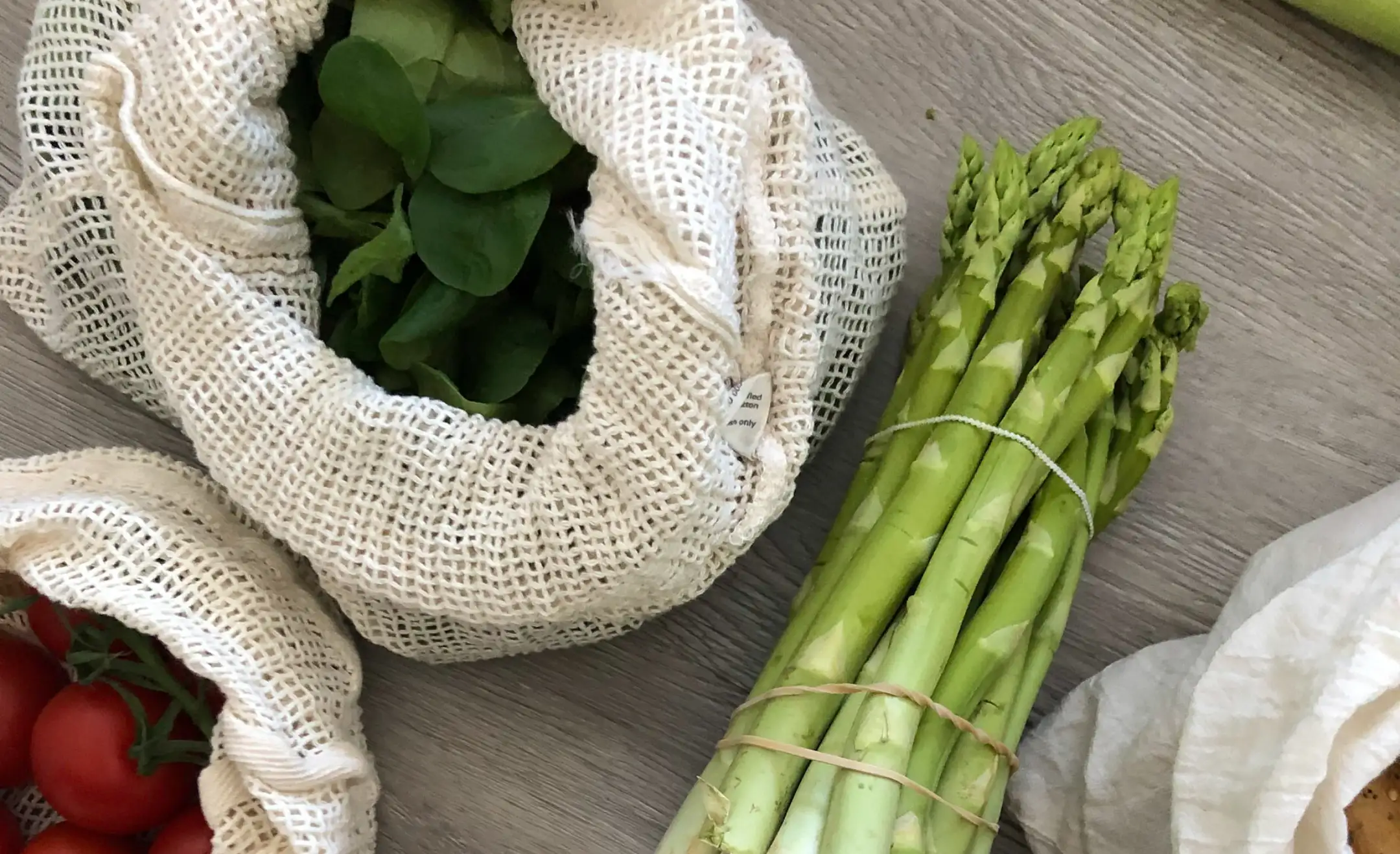 Verschiedenes Obst und Gemüse unverpackt vom Wochenmarkt. Spinat und Tomaten in Gemüsenetzen und daneben grüner Spargel.