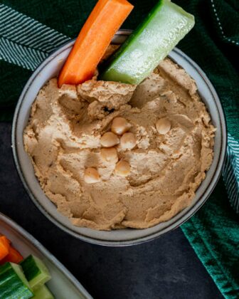 Blick aus der Vogelperspektive auf eine Schüssel mit Hummus. Im Hummus stecken Gemüsesticks.