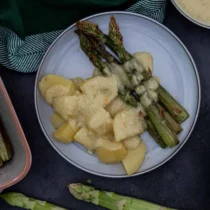 Auf einem Teller liegt grüner Spargel mit Kartoffeln und vegane Sauce Hollandaise.