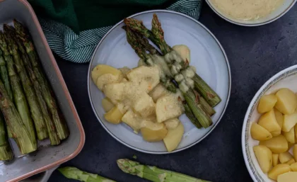 Auf einem Teller liegt grüner Spargel mit Kartoffeln und vegane Sauce Hollandaise.