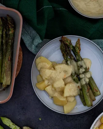 Auf einem Teller liegt das Ergebnis von dem veganem Spargel-Rezept: grüner Spargel mit Kartoffeln und veganer Sauce Hollandaise.