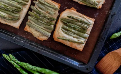 auf einem Backblech liegen fertige Spargel-Tartletts: Blätterteig-Quadrate, auf dem vegane Creme Fraîche und grüner Spargel ist.