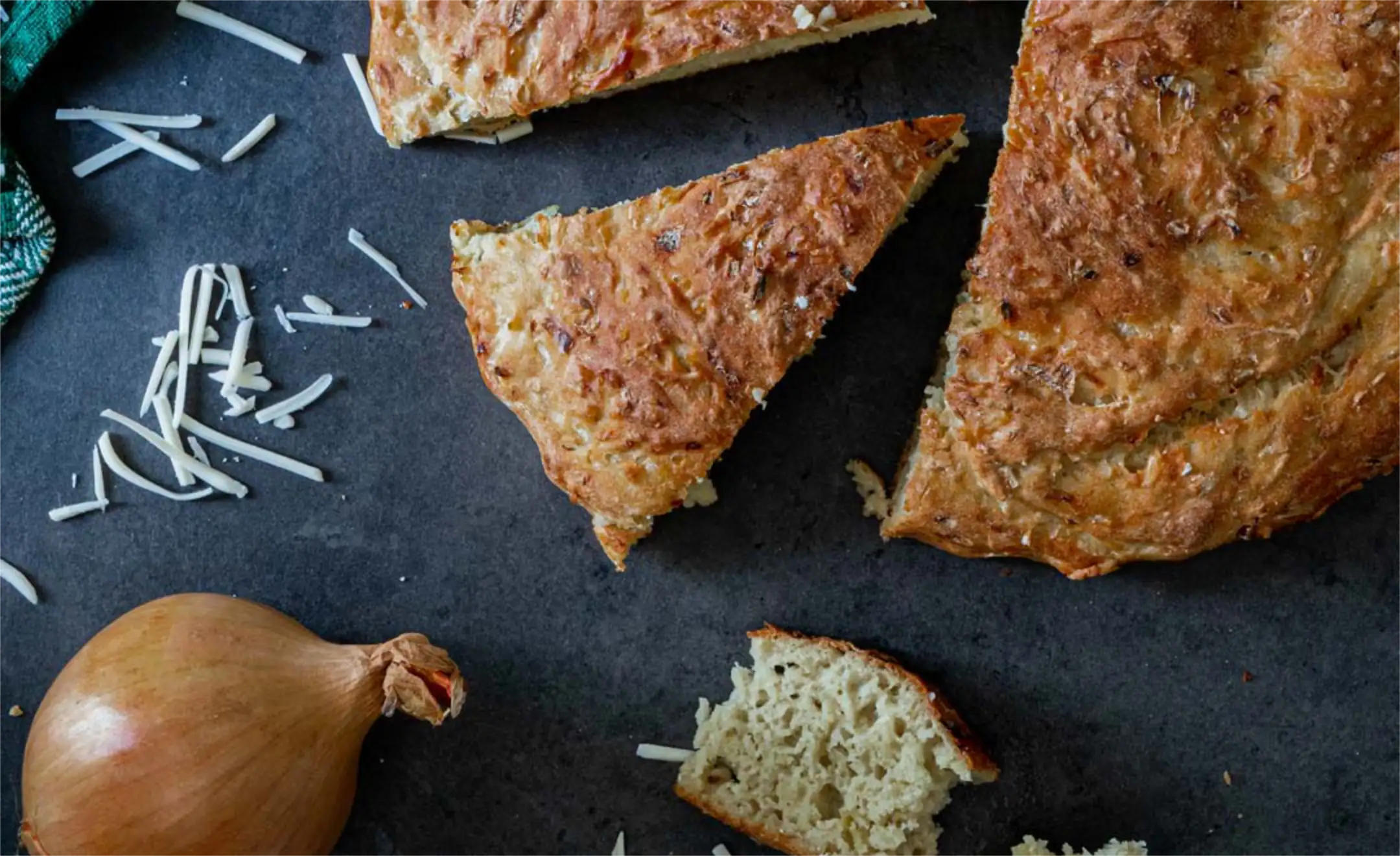 Veganes Grillbrot, dass angeschnitten ist. Daneben liegt zur Deko eine Zwiebel und Käse.