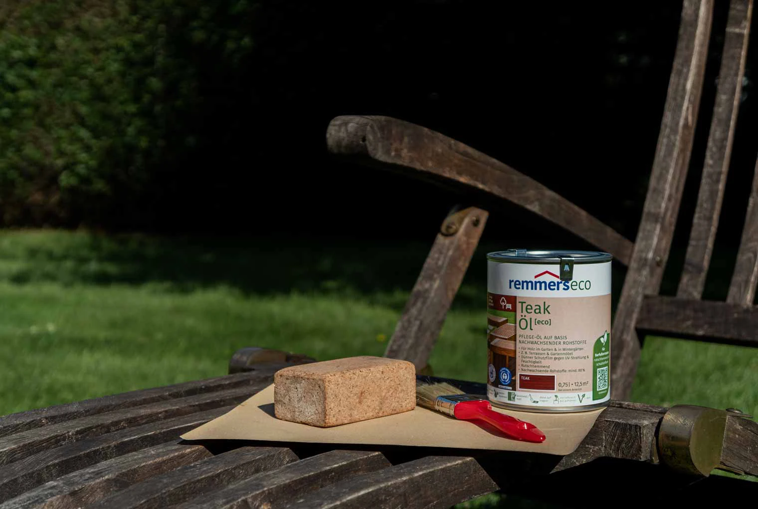 Auf dem Liegestuhl steht das Material um die Gartenmöbel zu streichen. Remmers Gartenholz eco Teak Öl, Pinsel und Schleifpapier.