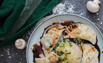 Pierogi auf einem Tell drapiert mit angebratenen Zwiebeln, Balsamico und Kräutern