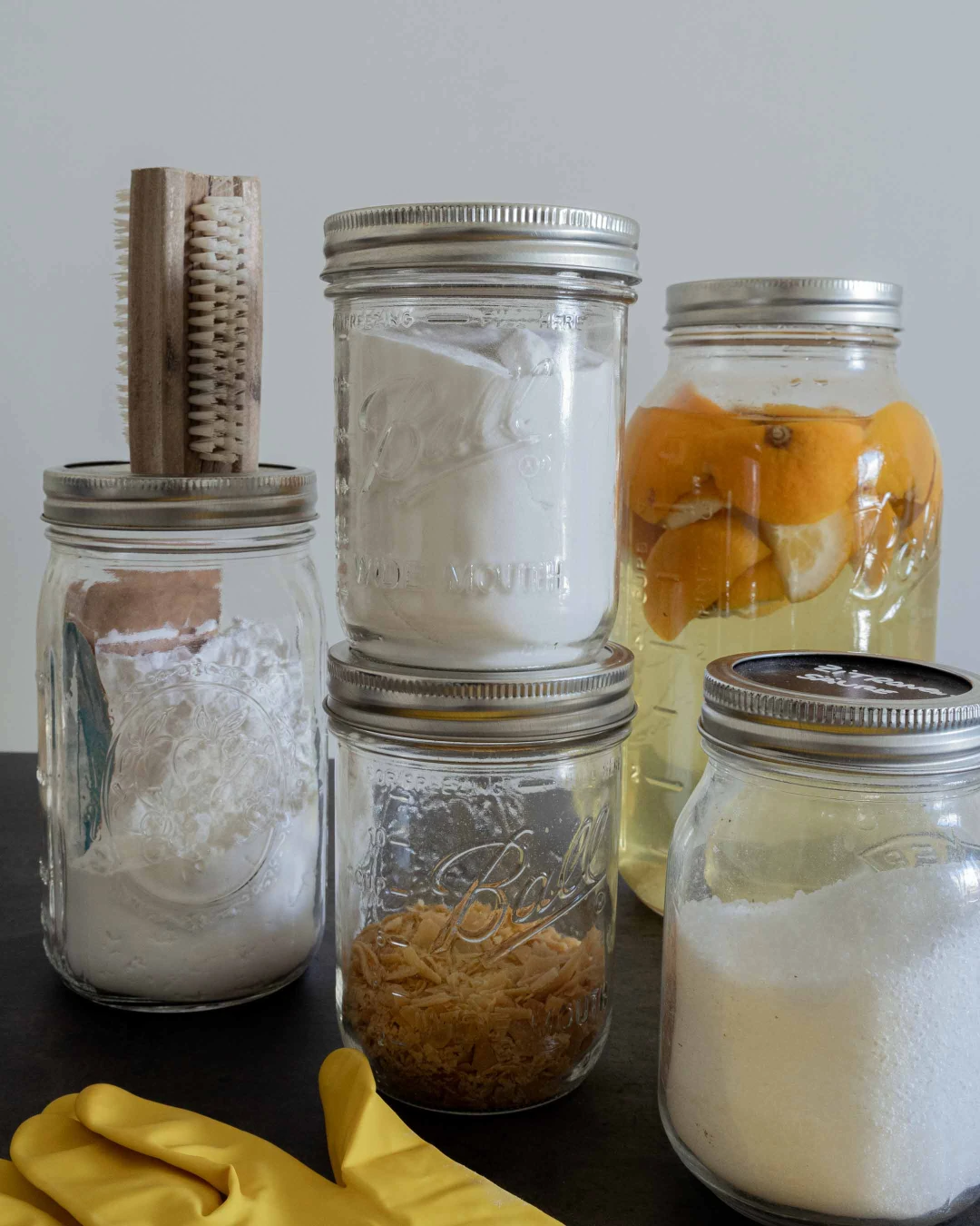 Fünf Hausmittel bestehend aus Natron, Soda, Kernseife, Essig und Zitronensäure in Gläsern