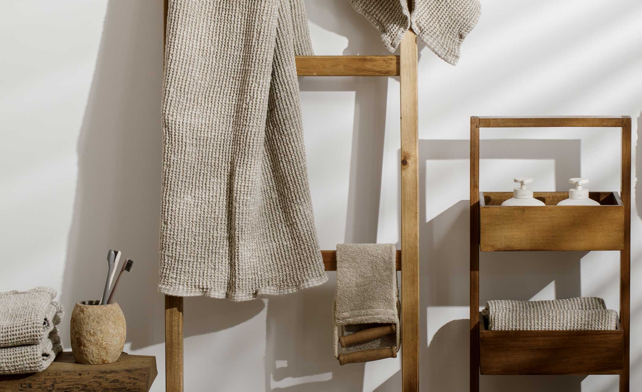 An einer Badezimmer-Wand steht eine Deko-Holzleiter mit Handtücher, daneben eine Bank und ein Regal mit weiteren Badezimmer-Produkten