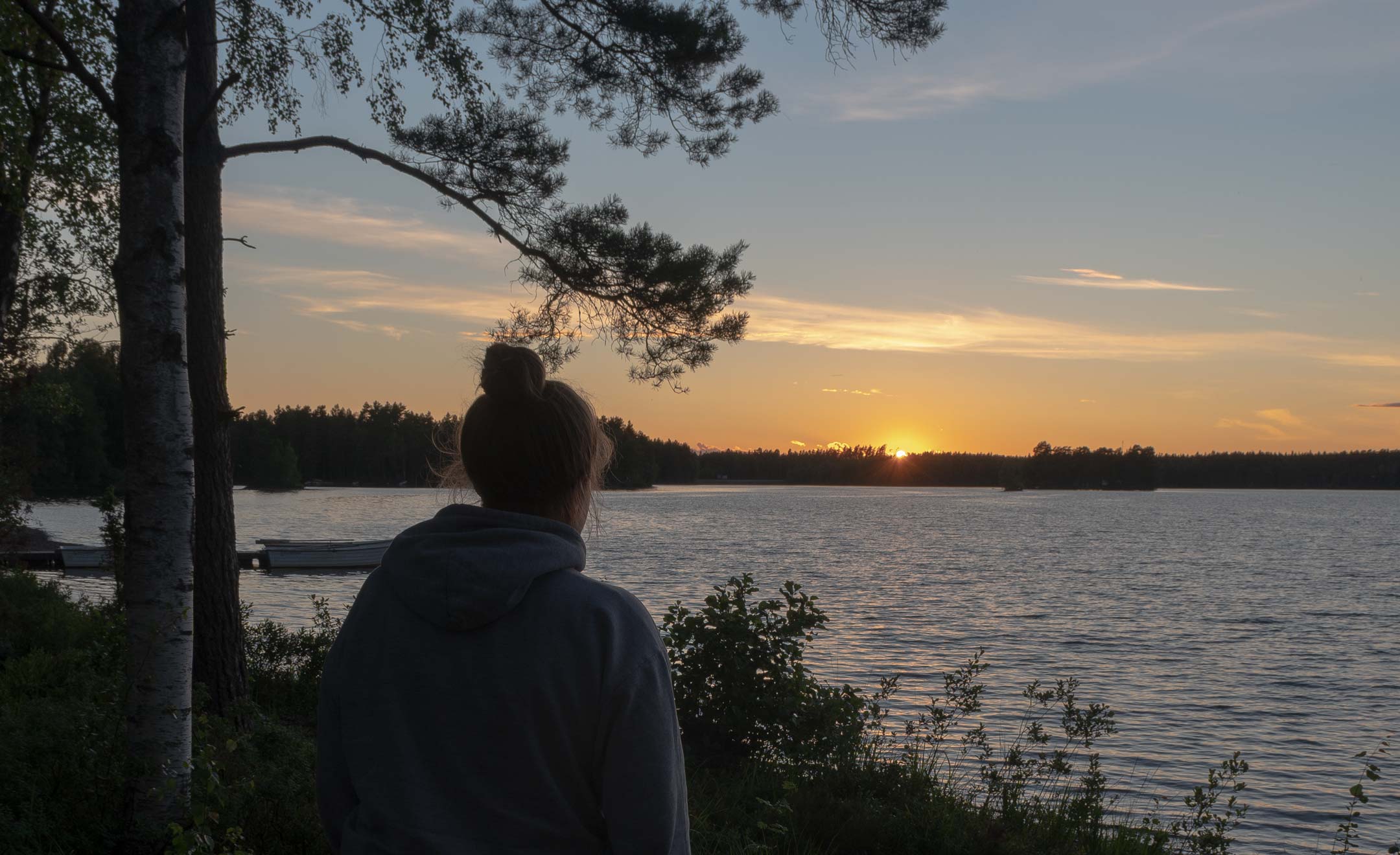 Annkathrin steht vor einem See mit Sonnenuntergang im Schweden-Urlaub. Auf dem Bild sieht man sie von hinten.