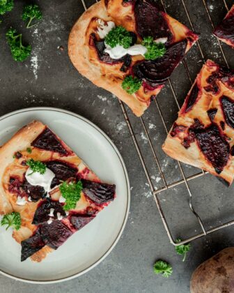 Stücke vom Flammkuchen mit Rote Beete Zwiebeln auf einem Teller.