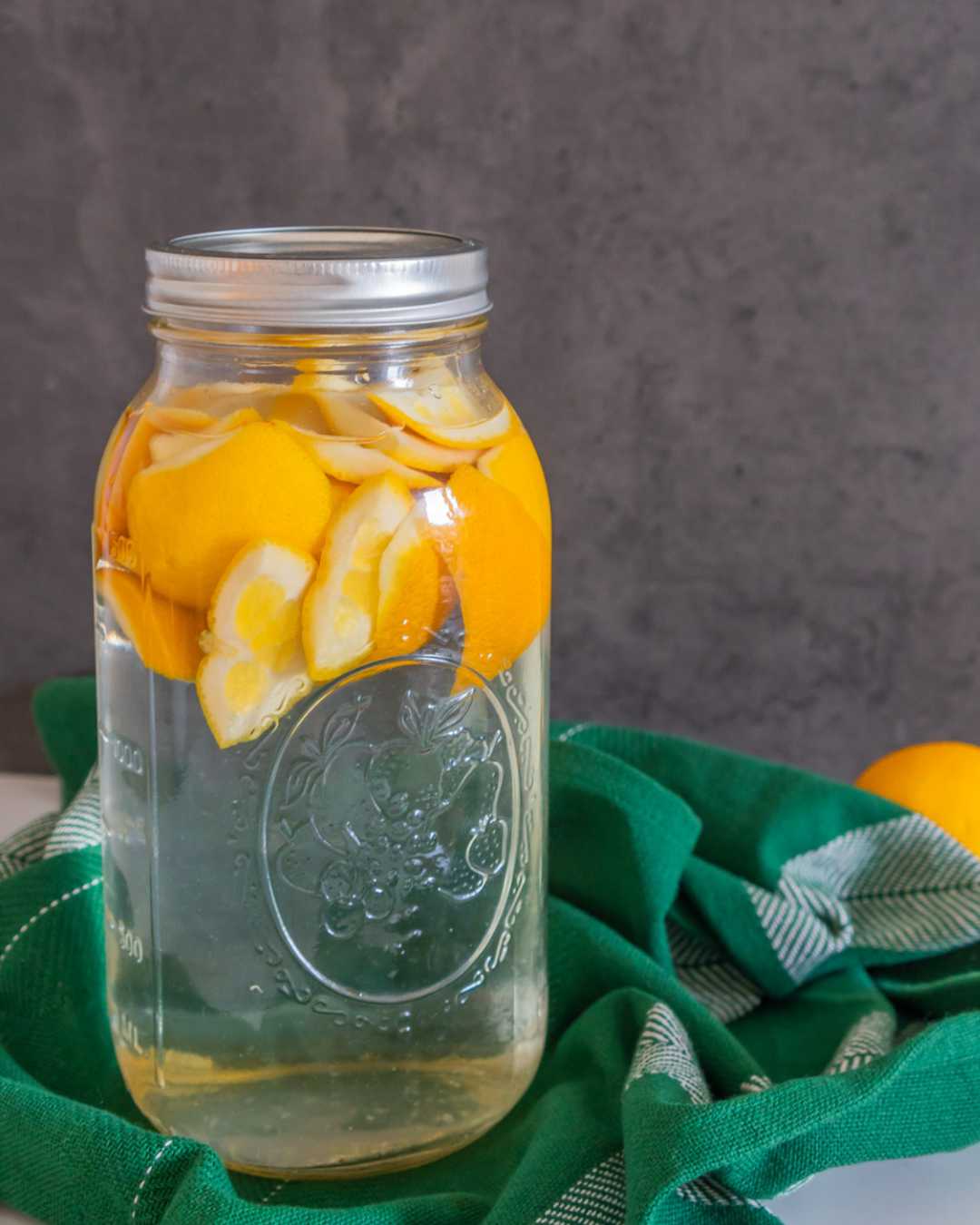 Essig und Orangenschalen in einem Glas, das zu Orangenreiniger wird.