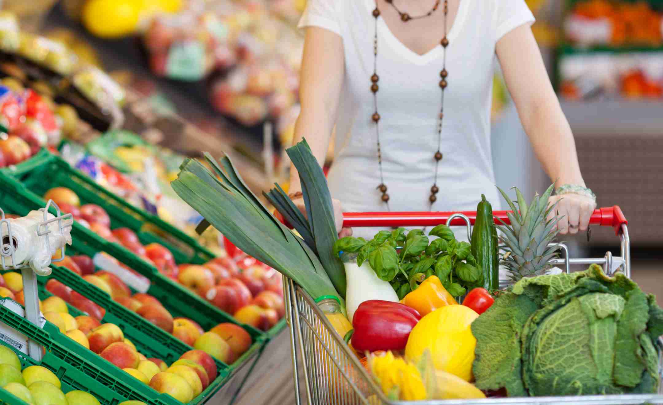 Eine Frau schiebt einen Einkaufswagen, der voll mit Obst und Gemüse ist im Supermarkt.