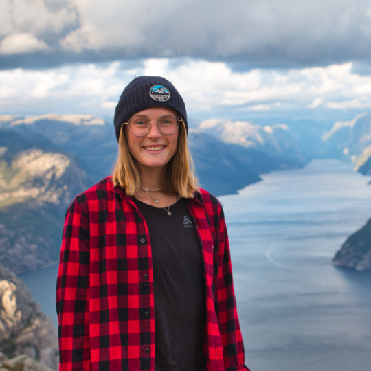Headshot von Steffi. Sie steht auf einem Berg, im Hintergrund ist ein Bergsee und Berge.
