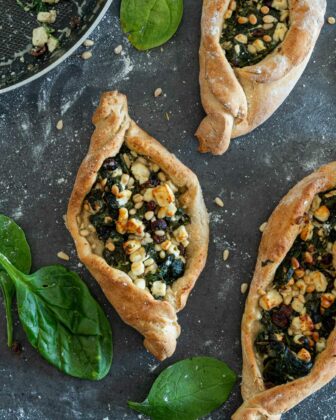 Vegetarische türkische Side mit Spinat und Feta von oben fotografiert. Drumherum liegen Spinatblätter und Pinienkerne.